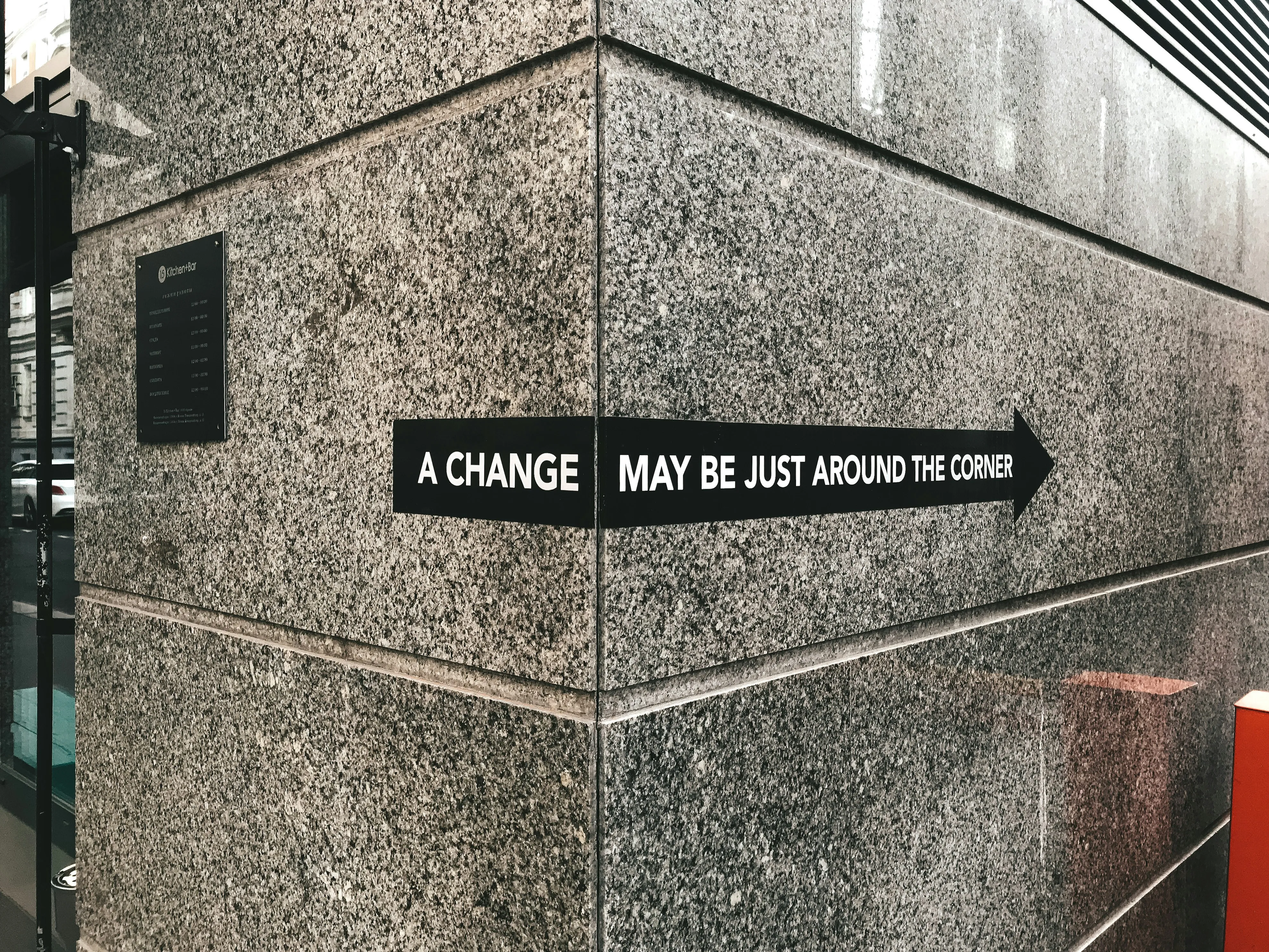 On the granite corner of a building, a black arrow sign reads: a change may be just around the corner.