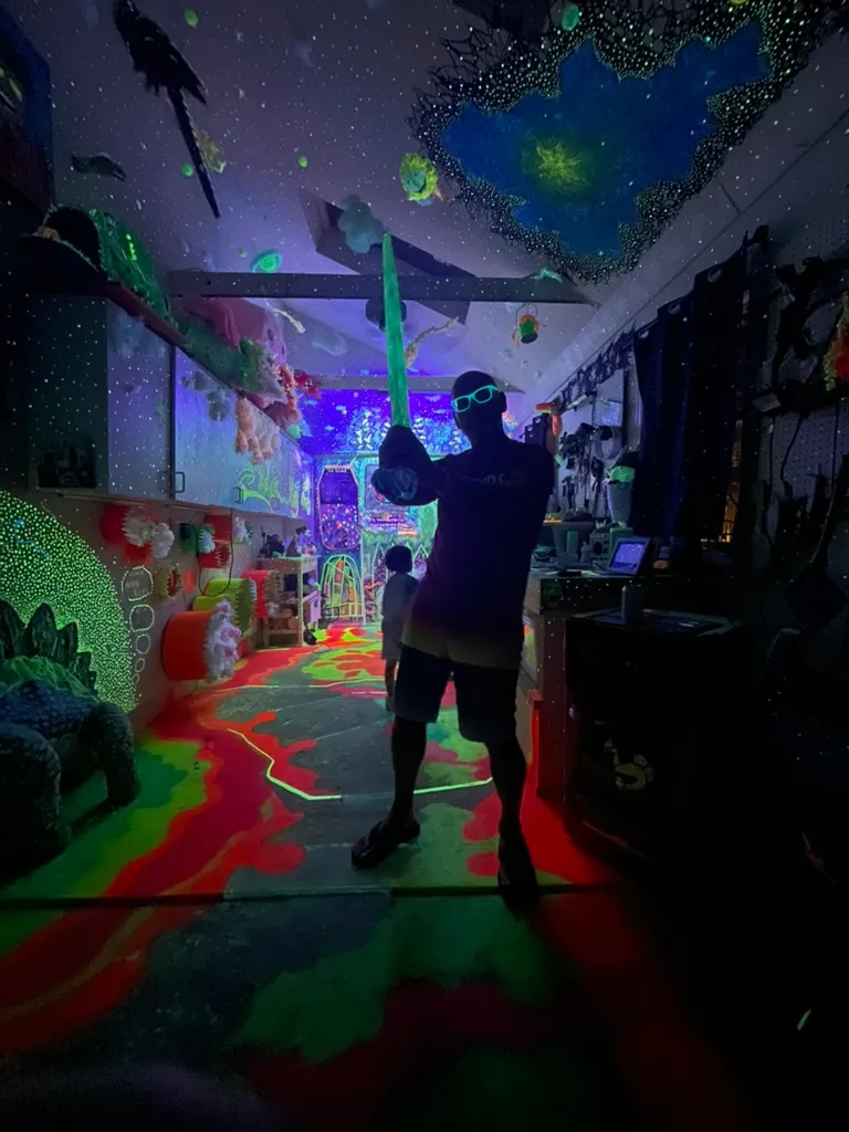 A darkened play room lit in green and pink, with a child and an adult in silhouette.